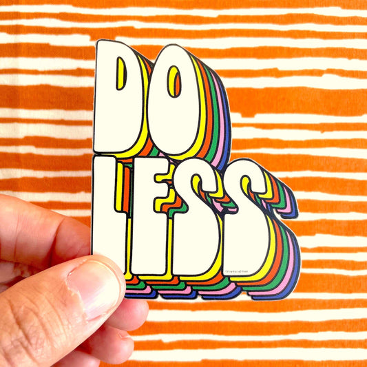 Fun "Do Less" vinyl decal sticker in retro rainbow lettering held in hand, perfect for laptops, notebooks, journals, and more.