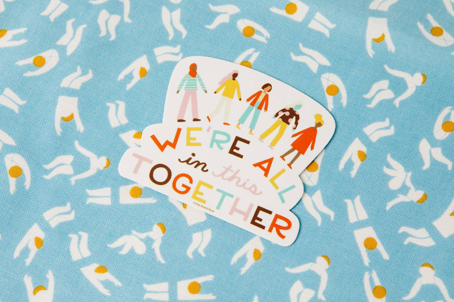 "We're All in This Together" vinyl decal sticker on a blue patterned background, perfect for laptops, water bottles, notebooks, and journaling accessories.