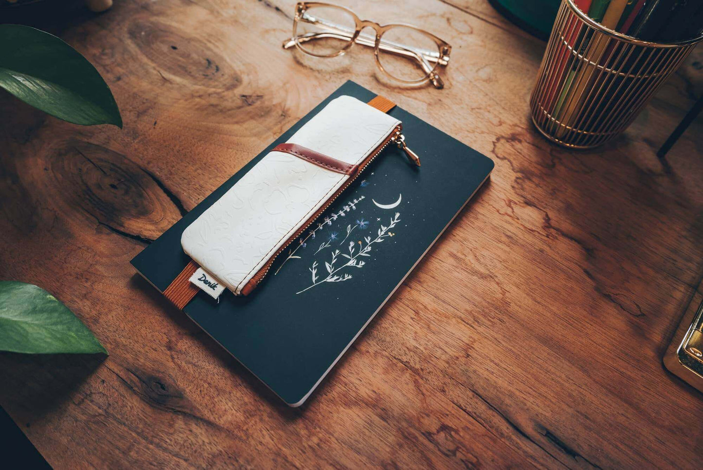 Golden Hour Embossed Vegan Leather Notebook Pouch on a wooden desk beside glasses and a plant, perfect for journaling.