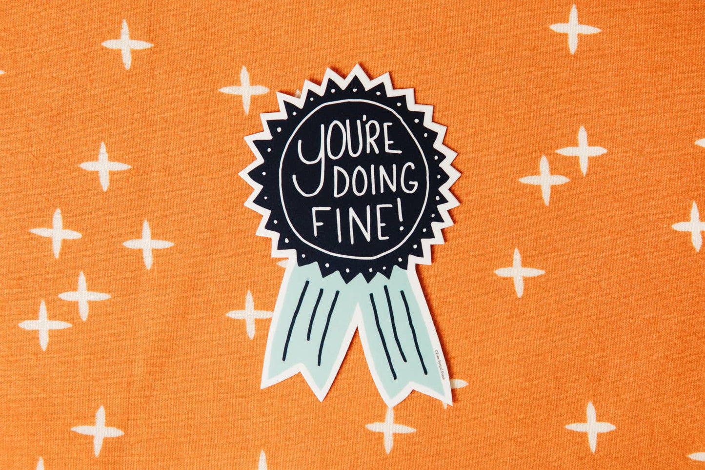 "You're Doing Fine vinyl decal sticker on a bright orange patterned background. Ideal for journals, laptops, water bottles, and more."