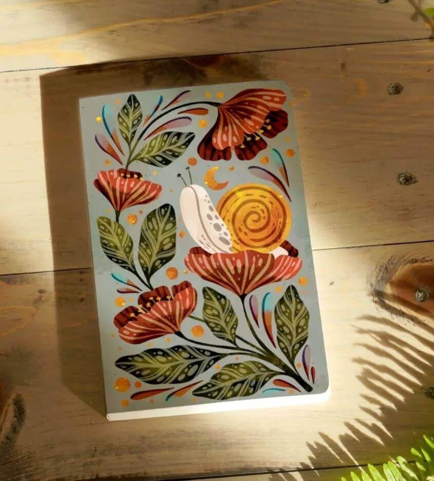 Moonlight Snail Classic Layflat Journal Notebook with vibrant floral cover basking in sunlight, perfect for journaling and guided prompts.