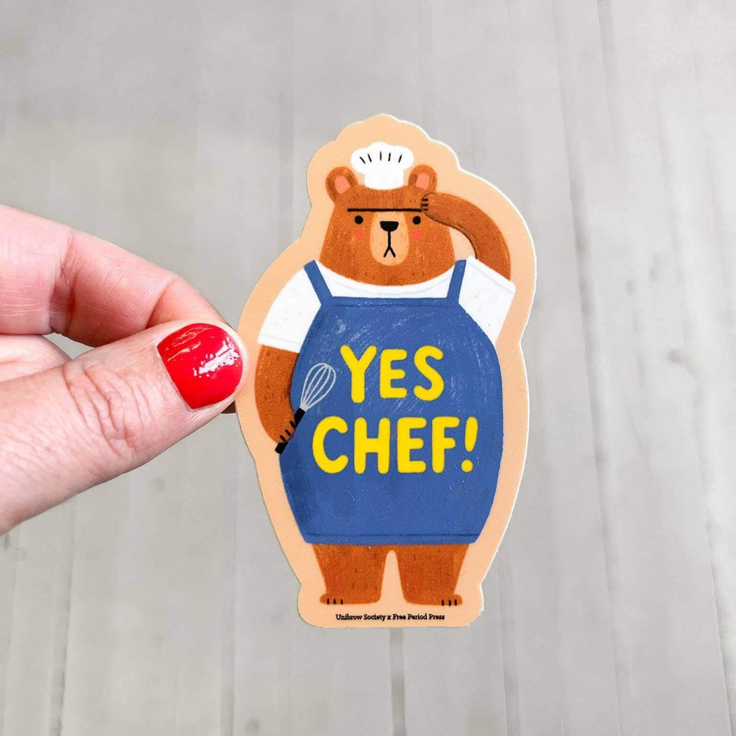 Hand holding 'Yes Chef Bear' vinyl decal sticker in kitchen; perfect for journaling, water bottles, laptops, and more cooking-themed fun.