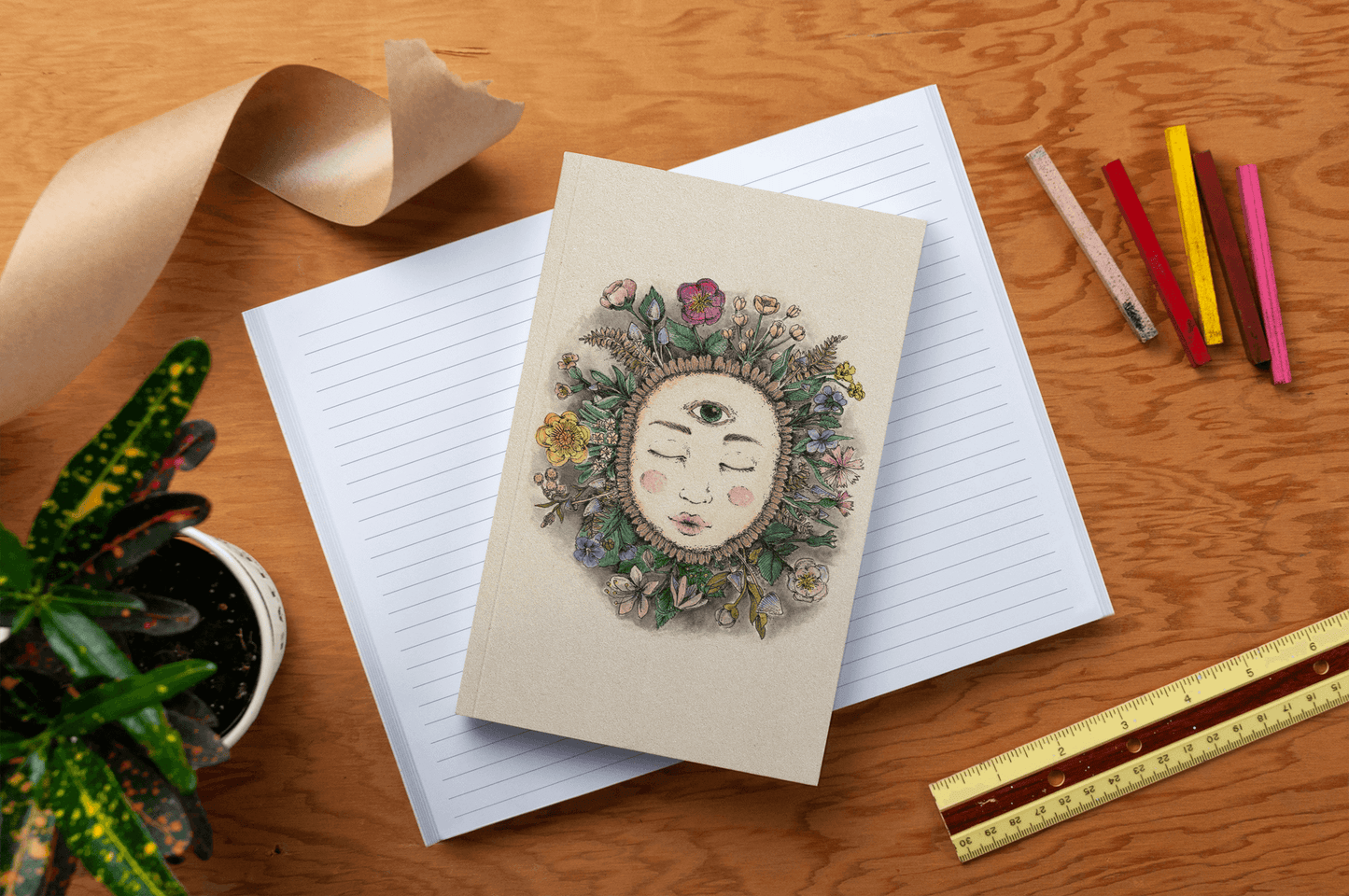 Earth Goddess Classic Layflat Journal Notebook with artistic floral cover on a wooden desk, accompanied by journaling supplies and plants.