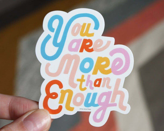 Colorful "You Are More Than Enough" vinyl decal sticker held between fingers, perfect for laptops, journals, and more.