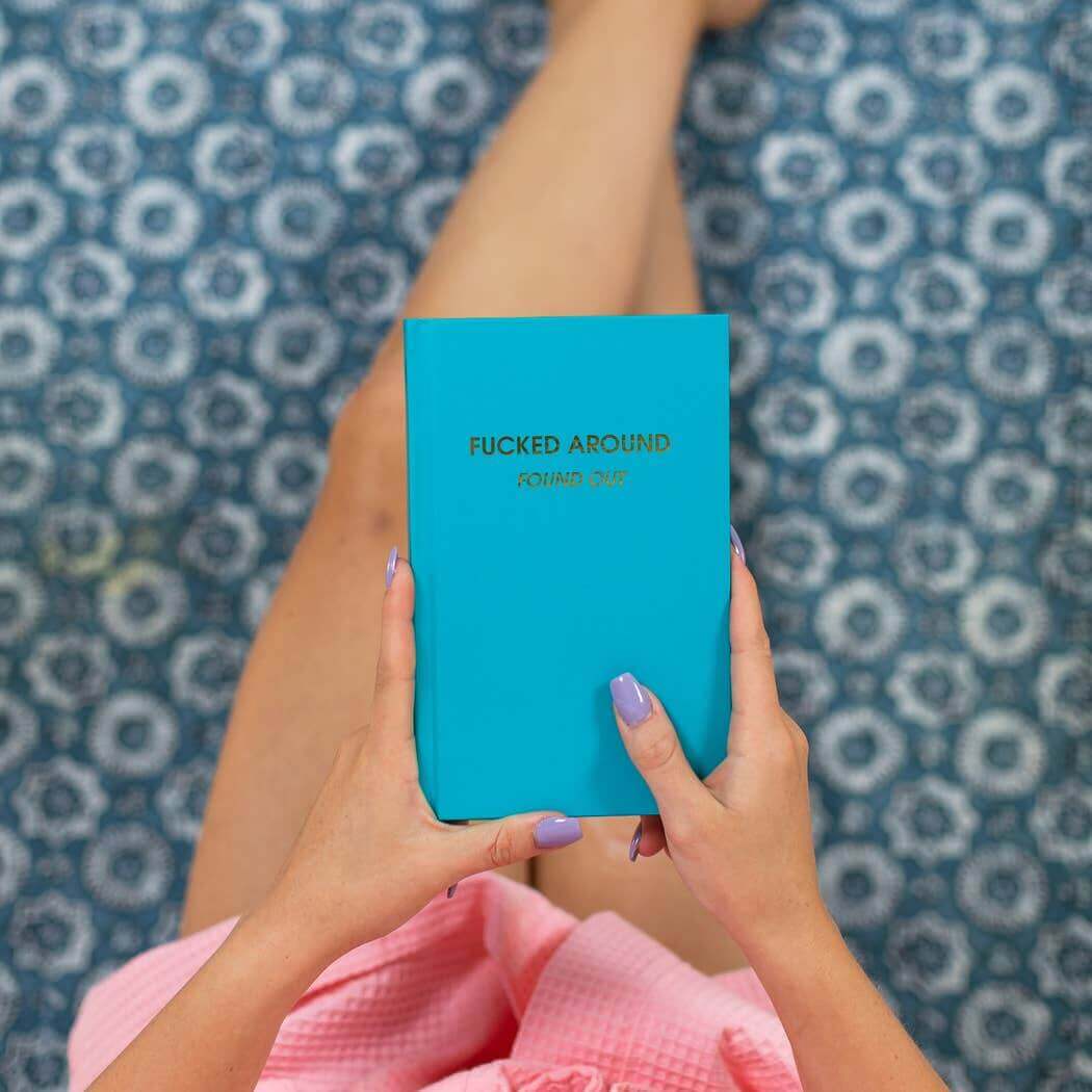 Person holding bright teal F***ed Around Found Out Journal with bold cover design, perfect for journaling and guided prompts.