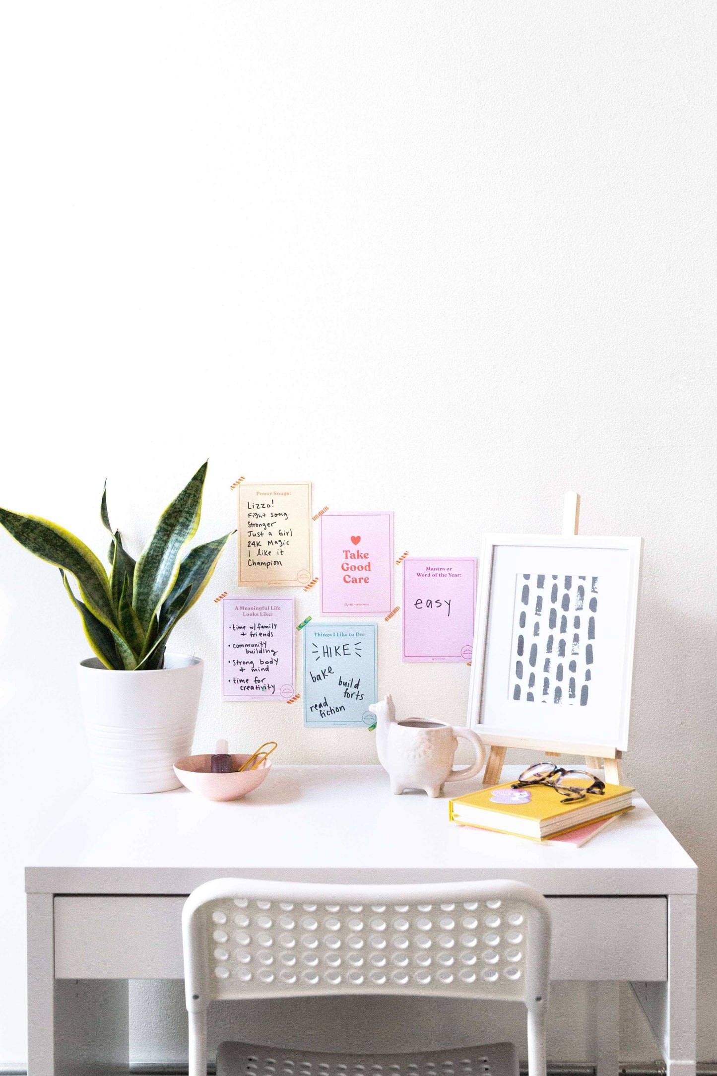 Cozy desk setup with self-care journal pages, a potted plant, a cup of tea, and a stack of books for inspirational journaling sessions.