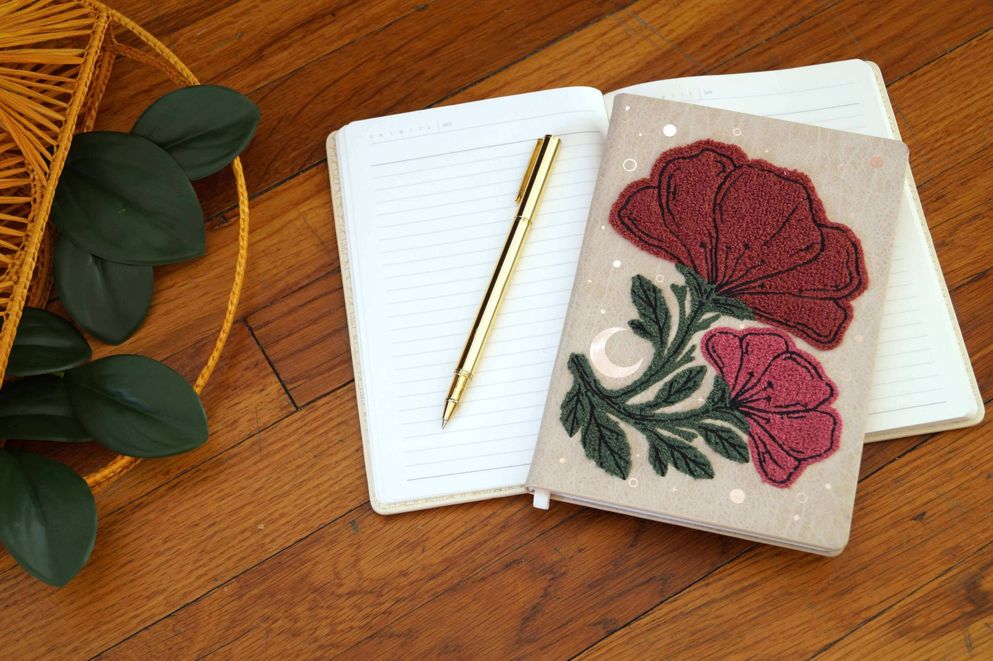 Double Bloom Embroidered Journal Notebook laying flat with pages open, featuring lined pages and a gold pen on a wooden surface.