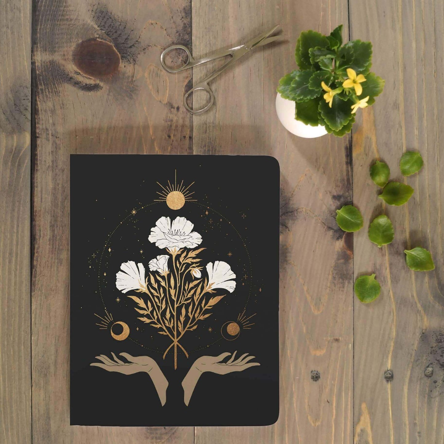 Celestial Flowers Medium Layflat Journal Notebook with water-resistant cover on wooden table, accompanied by journal supplies like scissors and plant.