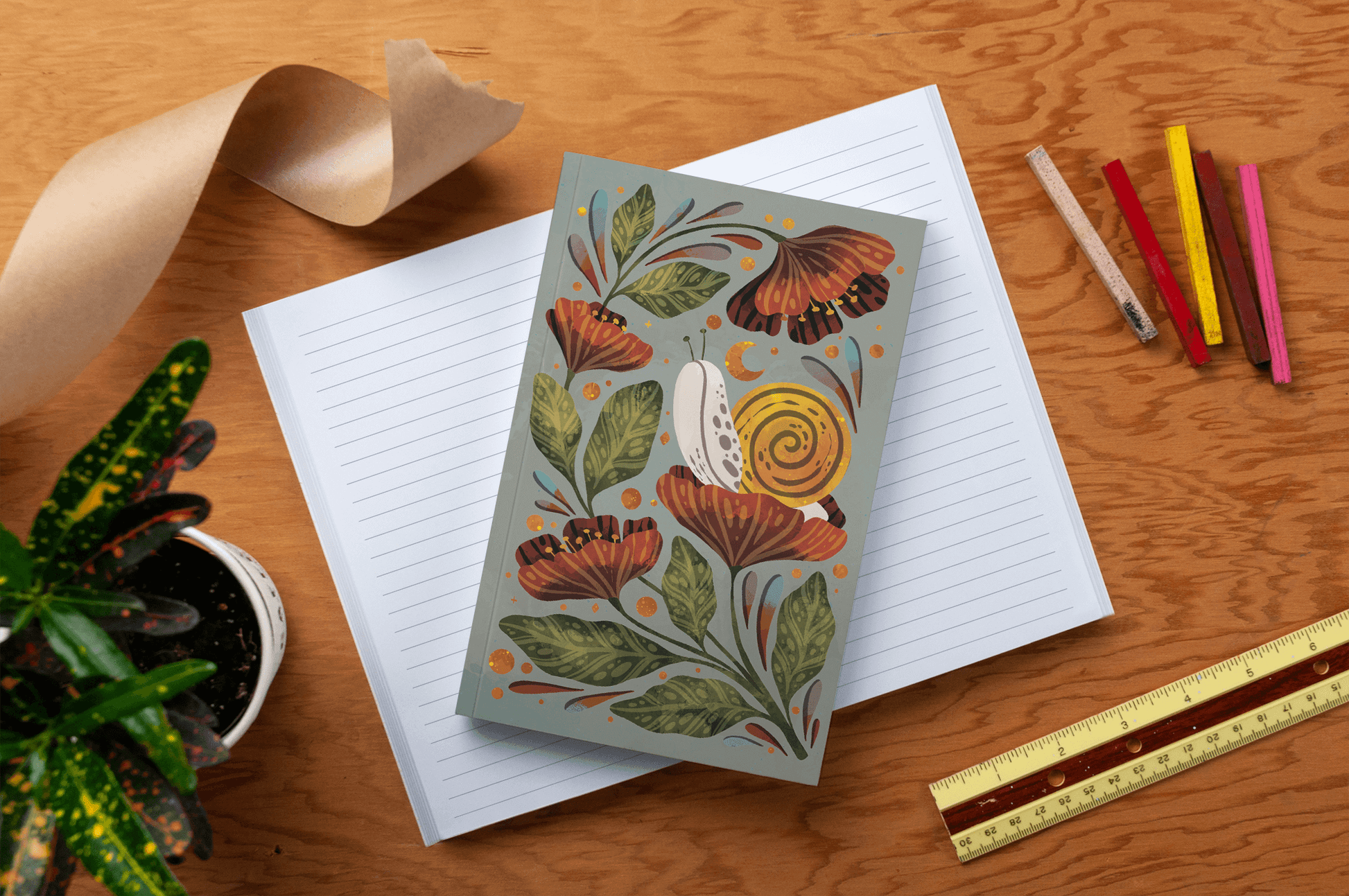 Moonlight Snail Classic Layflat Journal Notebook with colorful cover placed on an open lined journal with journaling supplies on wooden surface.