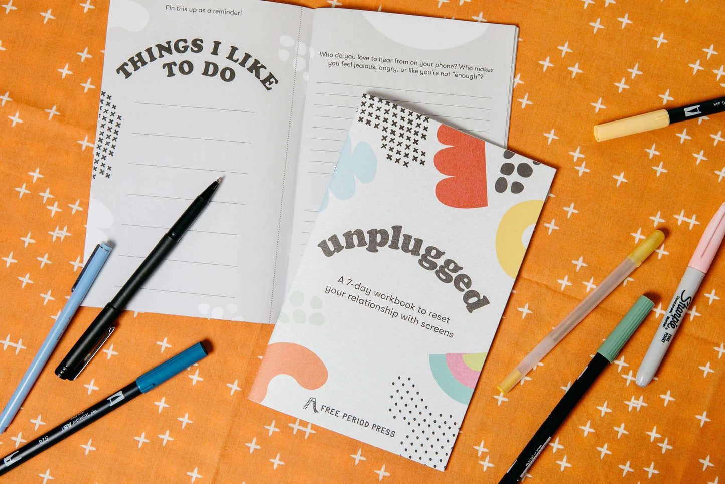 Workbook "Unplugged" with journal prompts, pens, and guided journaling supplies on orange patterned fabric.