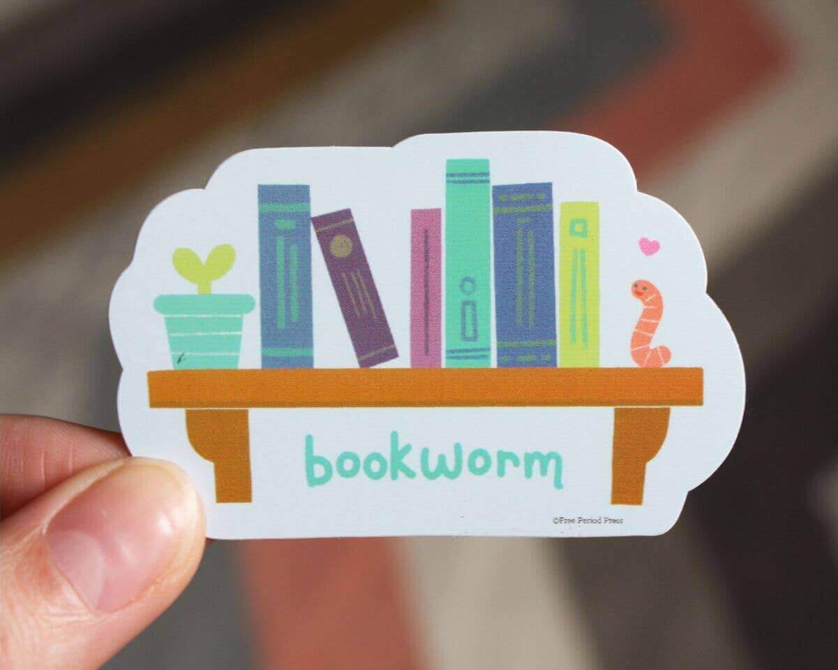 Hand holding Bookworm Vinyl Decal Sticker with bookshelf, books, plant, and bookworm illustration. Perfect for journals and journaling.