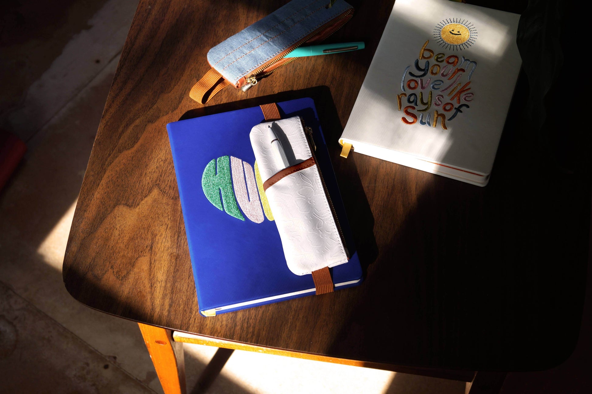 Embossed vegan leather notebook pouch on a wooden table with notebooks and journaling essentials in warm lighting.