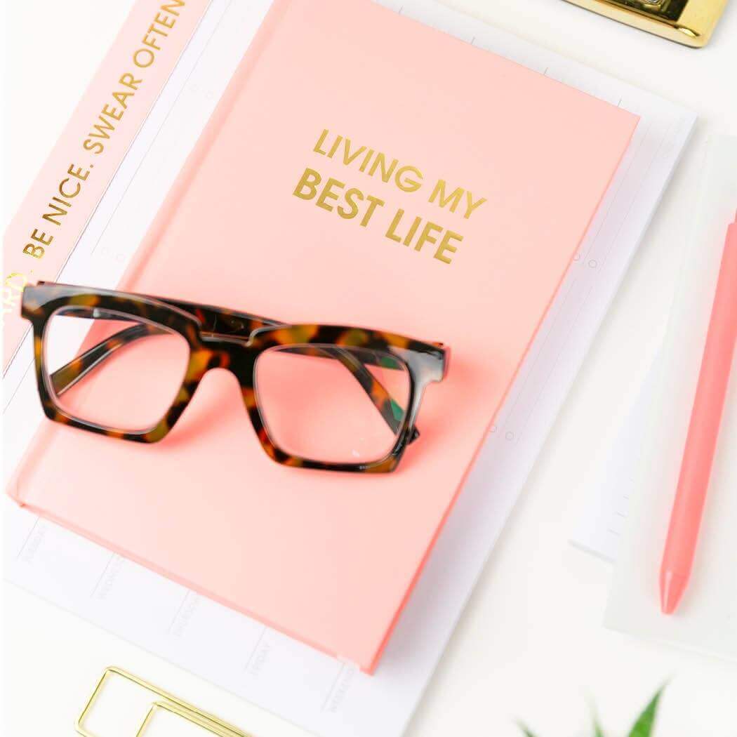 Stylish "Living My Best Life" journal with Bellini Pink cover, gold foil text, and glasses on top, perfect for journaling your best thoughts.