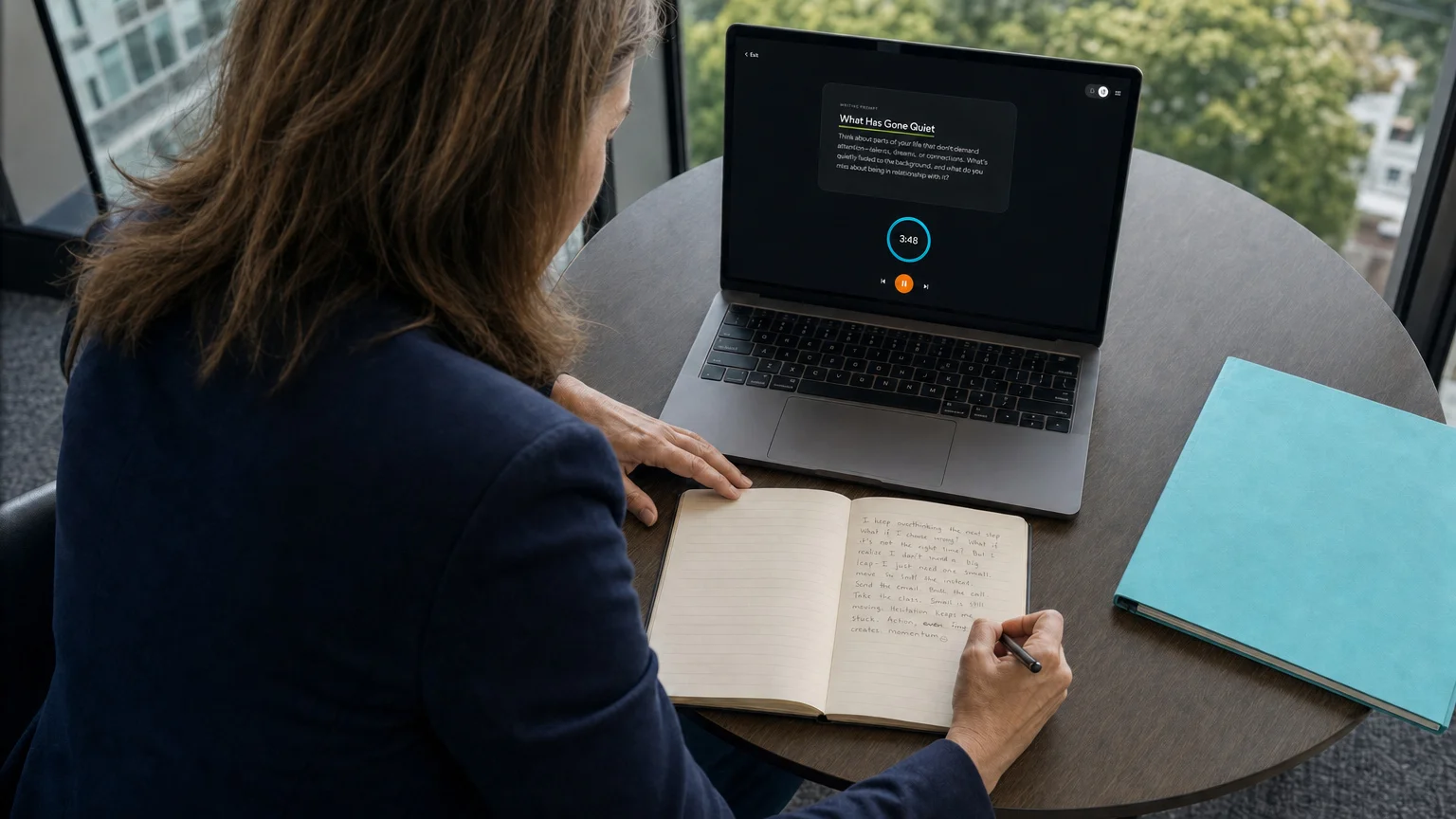 A client reflects in a journal at a desk with the guided session open on a laptop