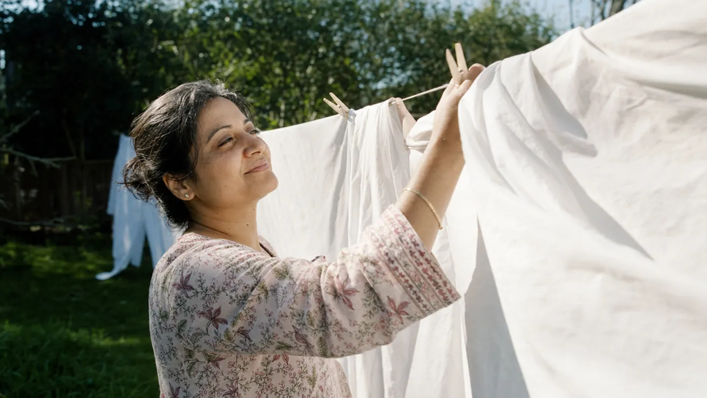 A woman hangs sheets on a clothesline and pauses as the breeze lifts them.
