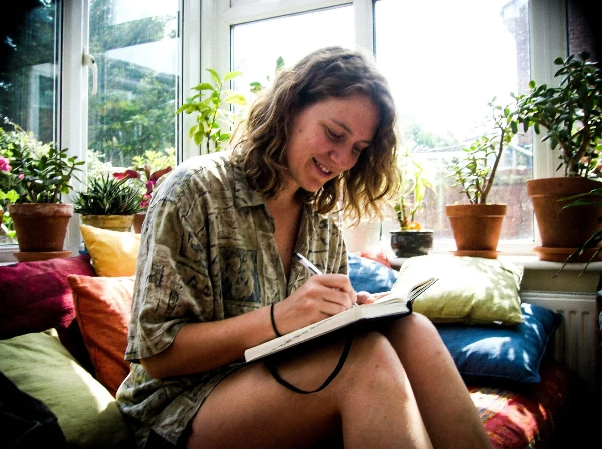 Person writing by hand in a paper journal in a bright sunroom